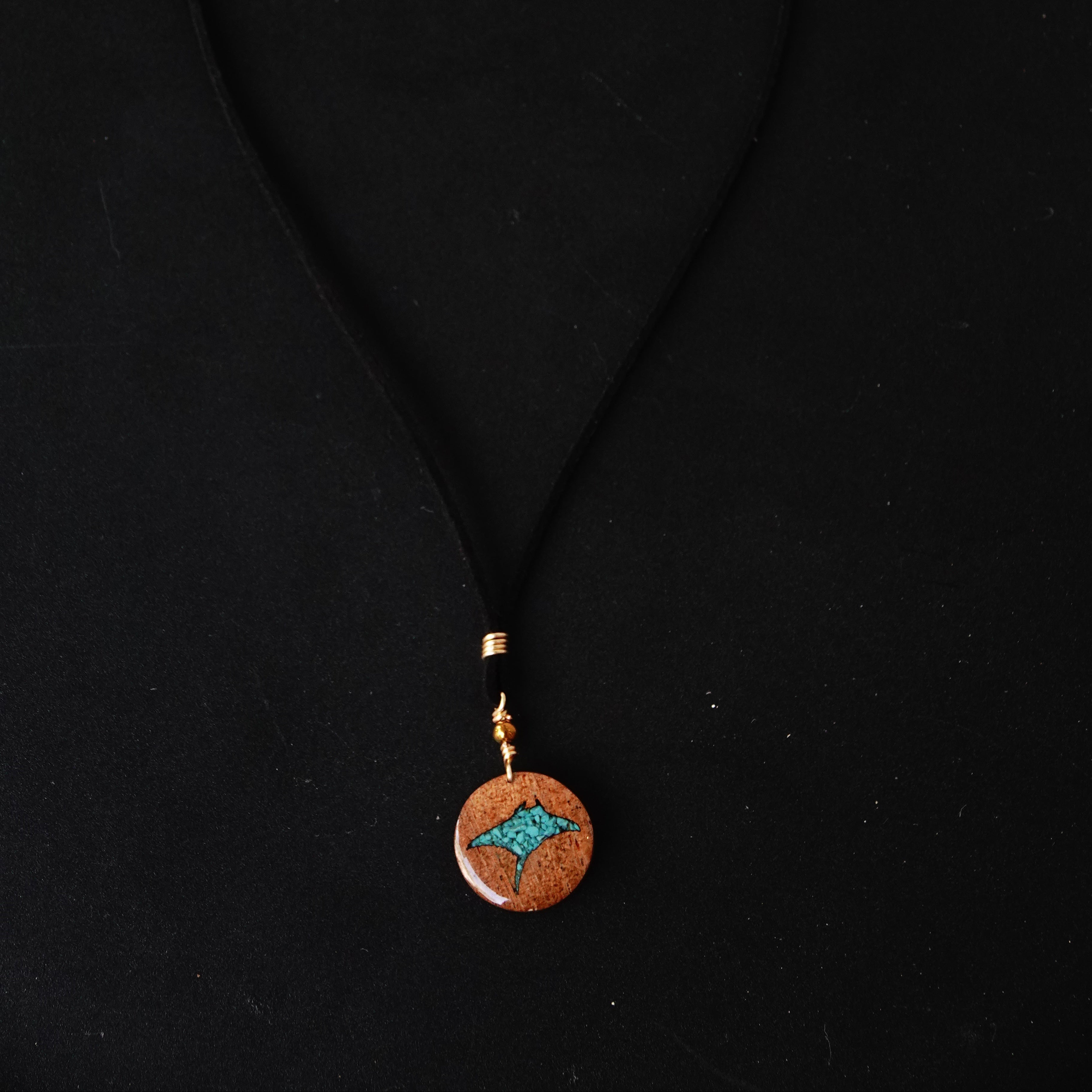 Round pendant with turquoise manta ray sand center and gold accents on a black background