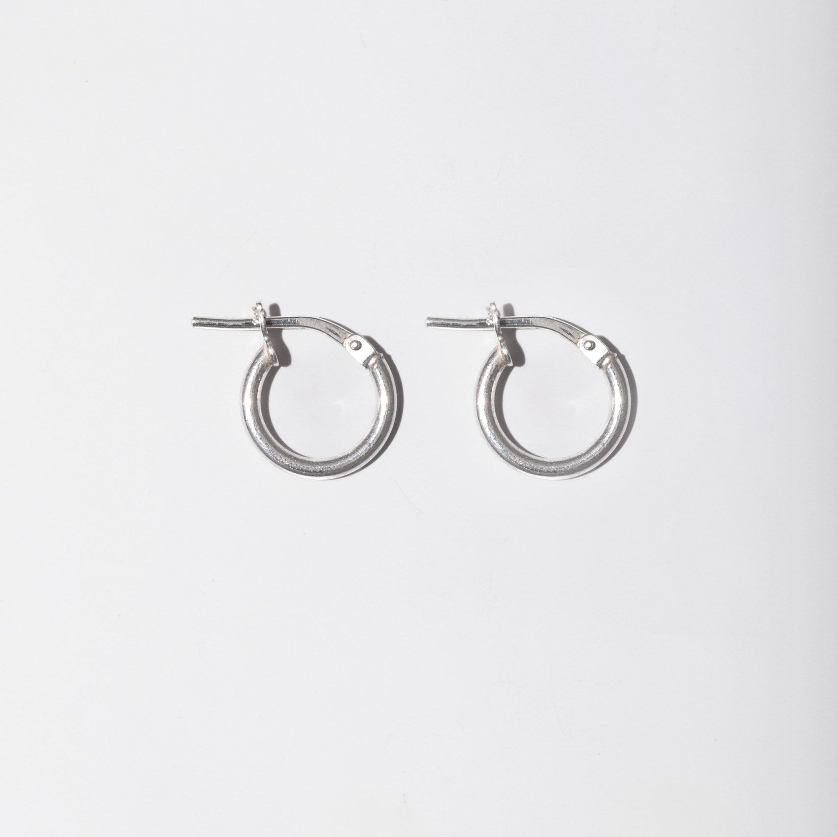 A pair of silver-toned metal hoop earrings with post backs, shown against a plain light gray background.