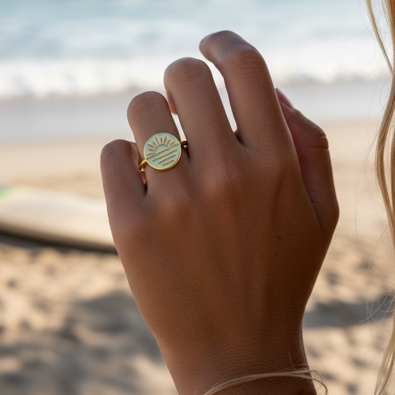 Hand wearing a gold ring with a beach in the background