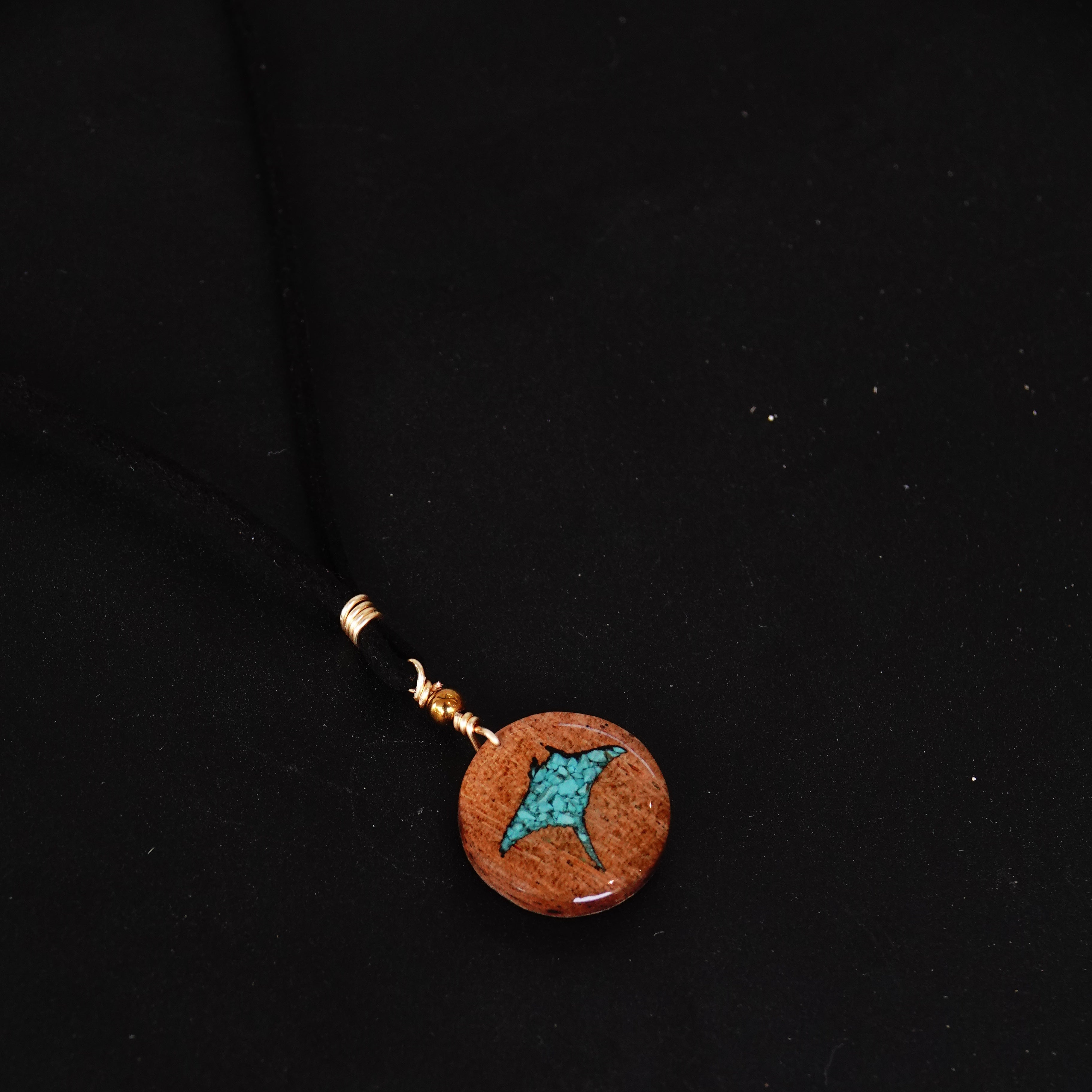 Round pendant with turquoise manta ray center and gold accents on a black background