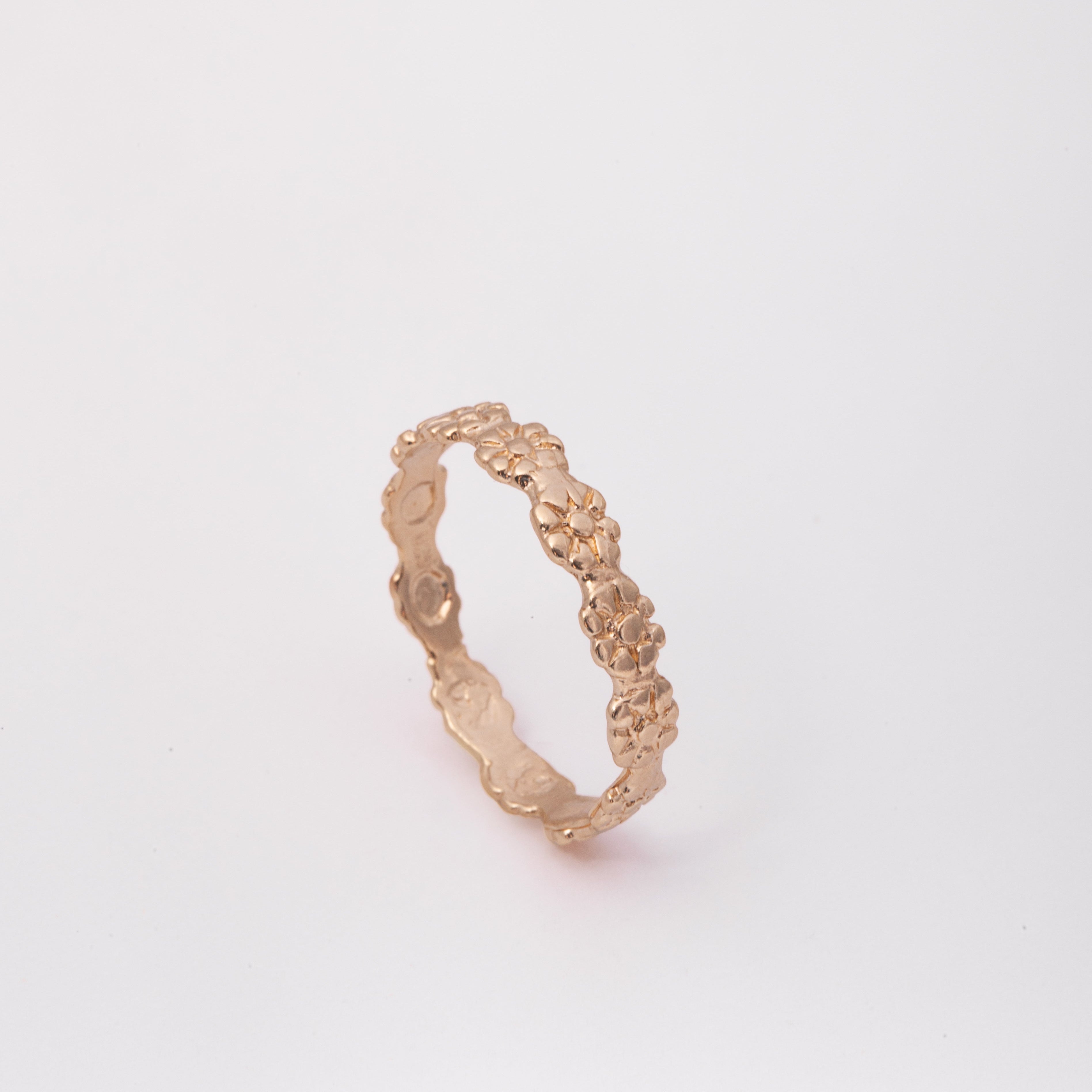 A textured rose gold band ring with a wavy, organic surface pattern, photographed on a seamless light gray background.