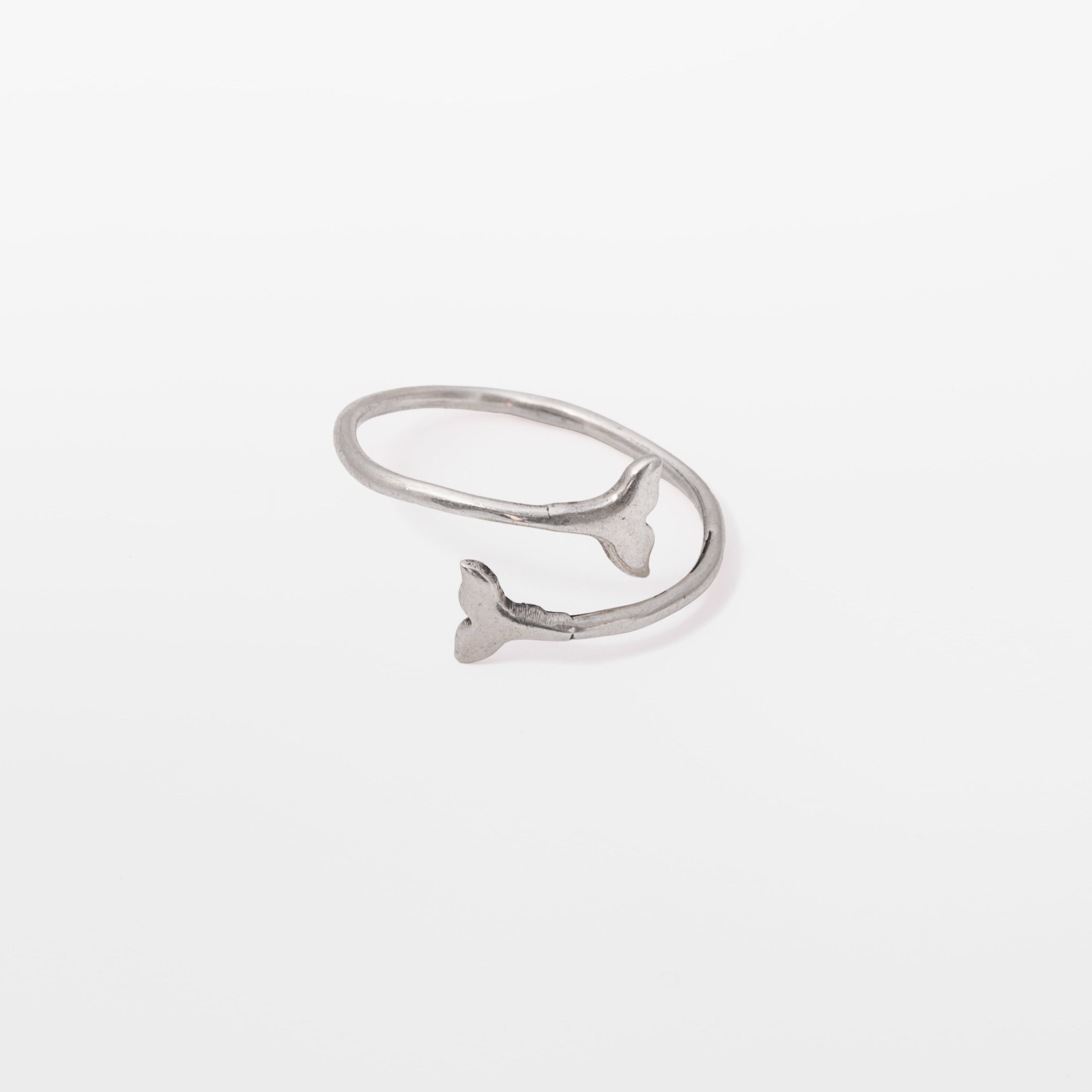 A silver open ring band featuring a small fish tail charm on one side, photographed against a seamless white background.