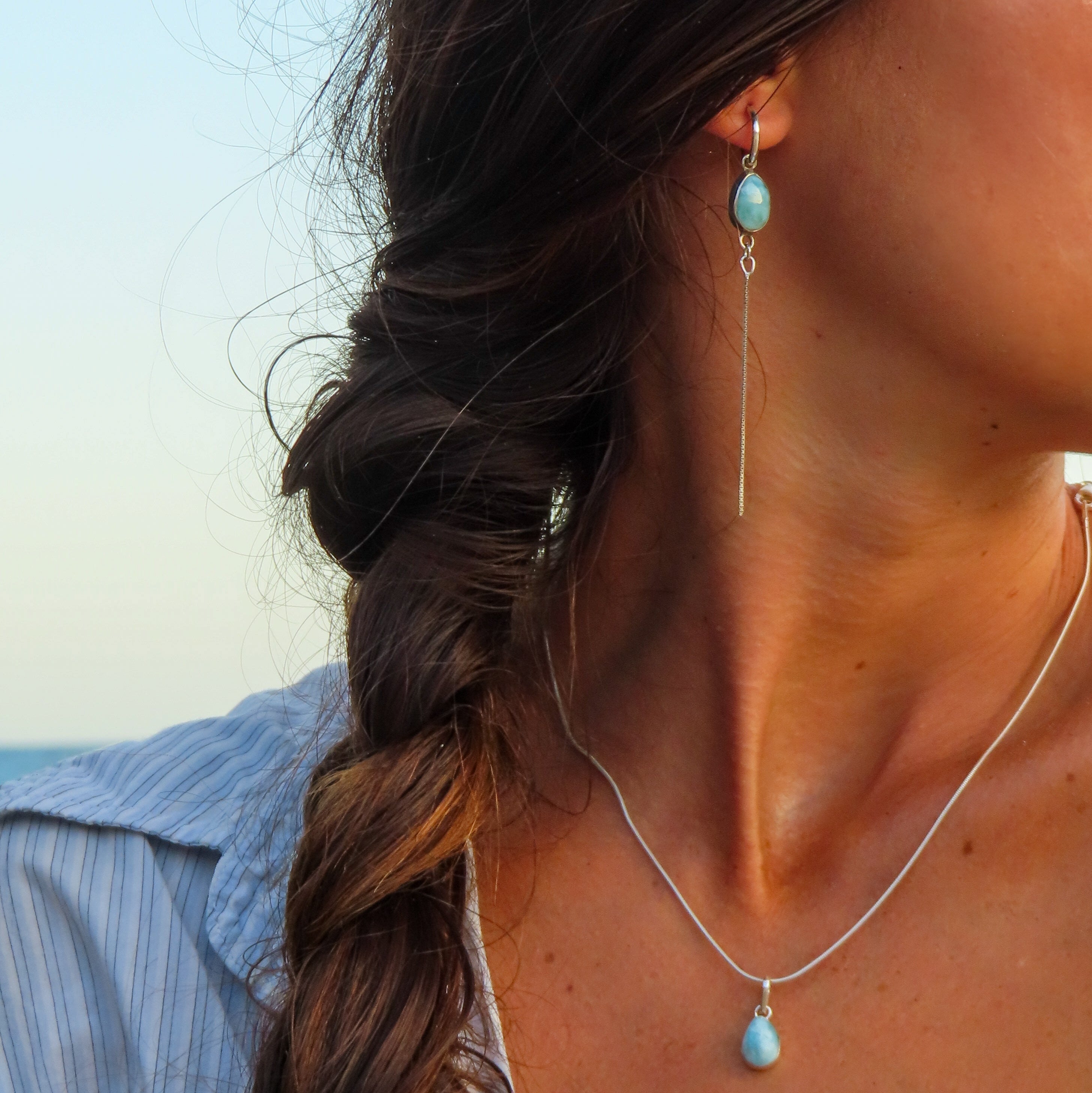 Woman with braided hair wearing turquoise earrings and a necklace against a blurred natural background