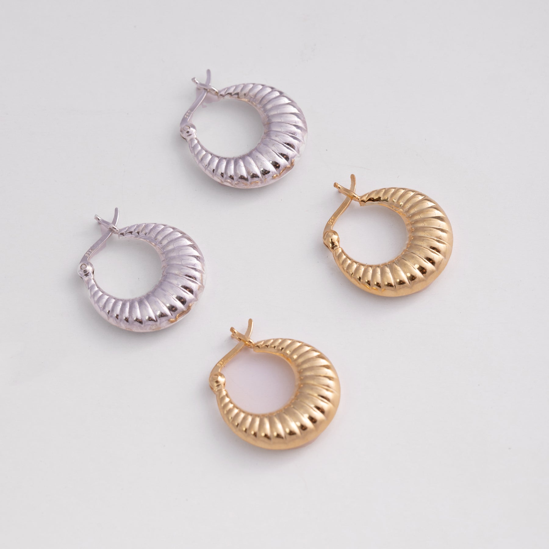 Set of four hoop earrings in gold and silver on a light gray background