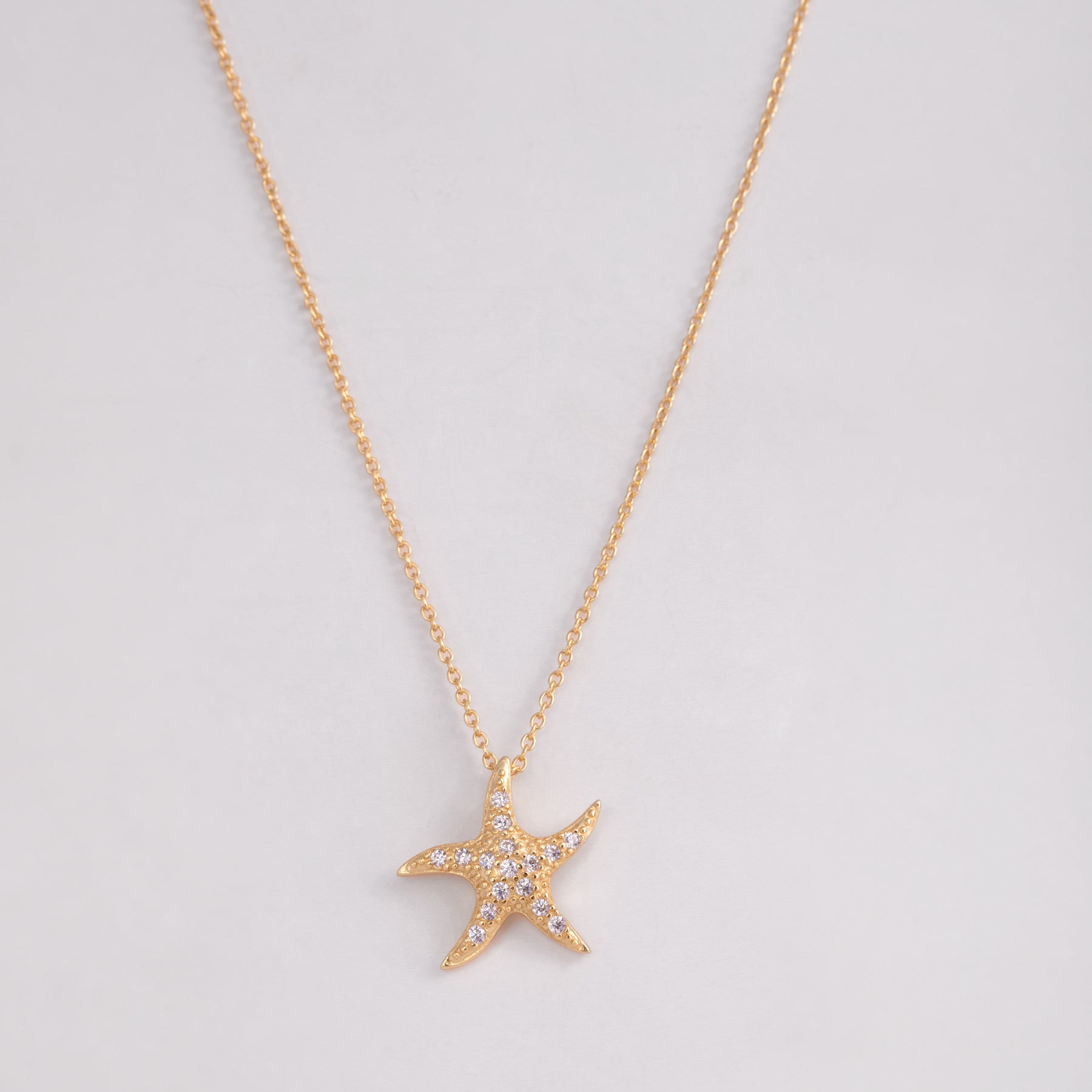 A gold-plated necklace with a pendant shaped like a starfish, displayed against a light background.