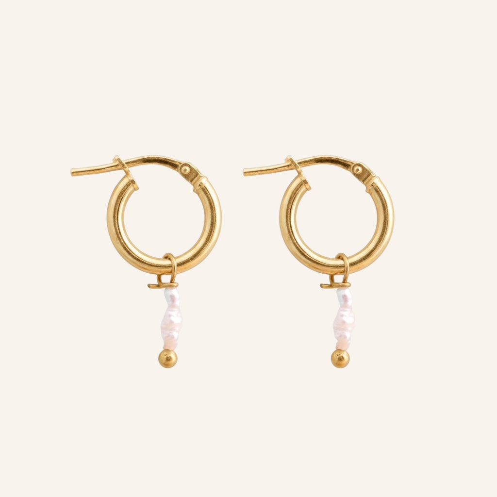 Gold hoop earrings with pearl-like bead drops on a beige background